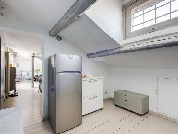 A modern kitchen with a stainless steel refrigerator, white cabinetry, and a wooden floor.