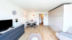 A modern living room with a flat-screen TV, a dining table with chairs, a sofa, and a large wardrobe. - Studio in Wenduine Near the Beach (De Haan)