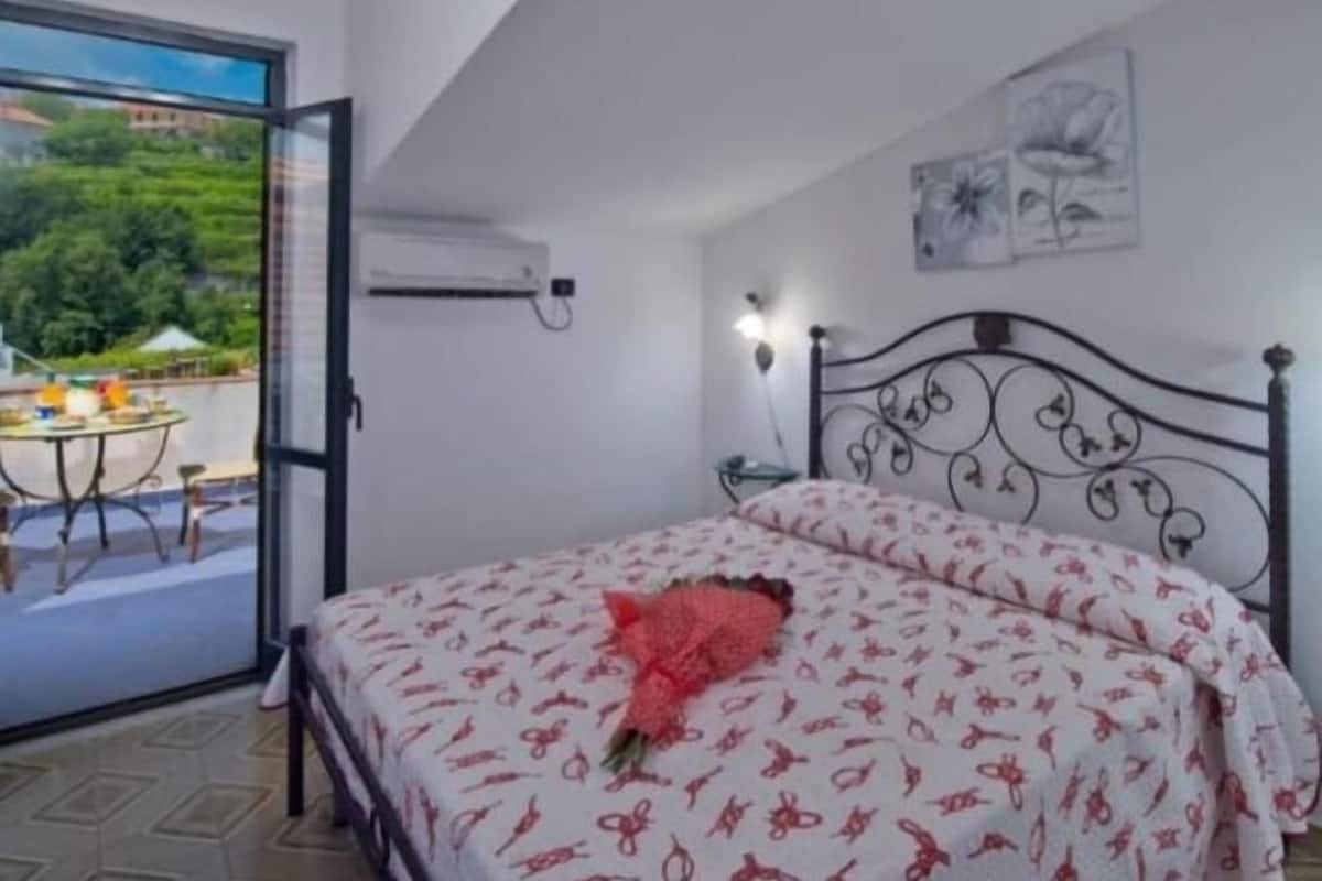 A bedroom with a bed, a window, and a view of greenery outside.