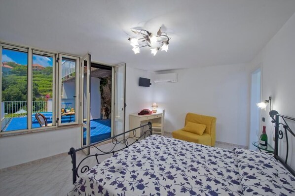 Une chambre à coucher avec un lit, une chaise jaune, un bureau et une vue sur une piscine.