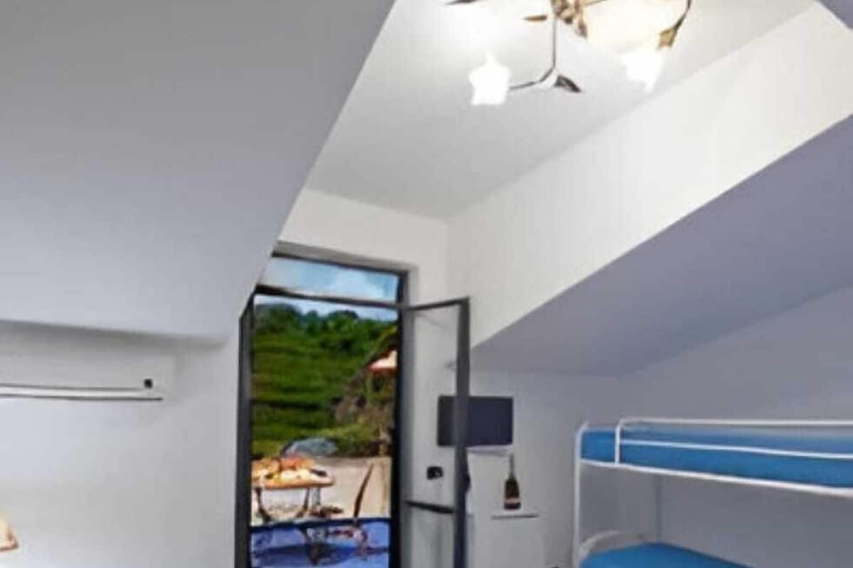 A bedroom with a bunk bed, a bedside table with a lamp, and a window overlooking a garden.