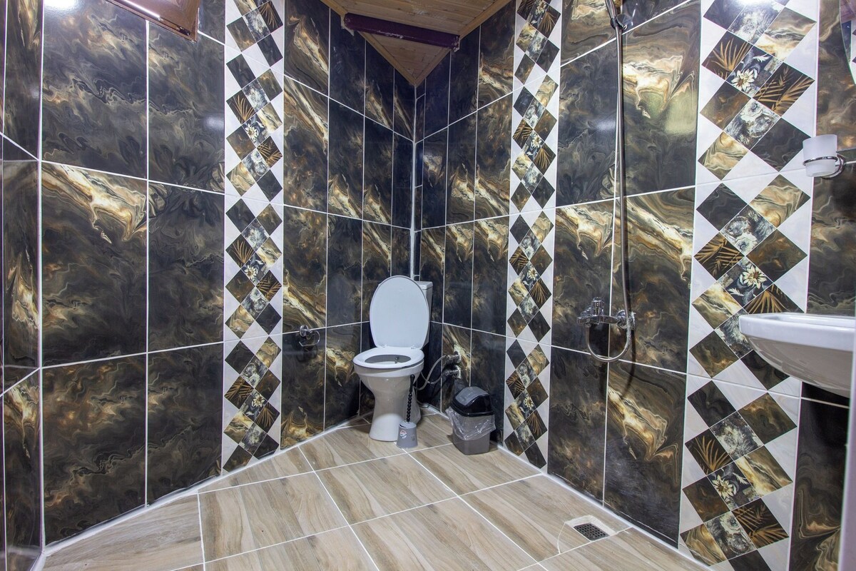 A bathroom with a toilet, shower, and sink. The walls are tiled with a marble pattern.