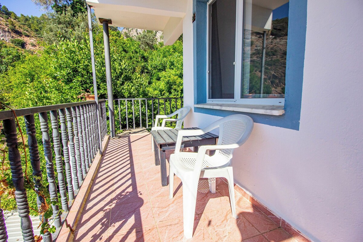 A balcony with a table and chairs, a railing, and a view of greenery.