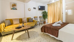 Una habitación de hotel acogedora con sofá, cama, televisión, planta y mesa de comedor.