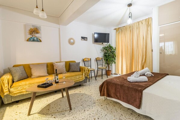 Una habitación de hotel acogedora con sofá, cama, televisión, planta y mesa de comedor.