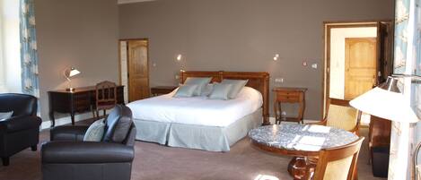 A bedroom with a bed, a desk, a chair, a table, and a lamp.