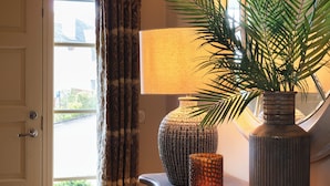 A room with a door, a window with curtains, a lamp, and a potted plant.