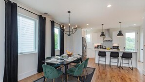 A modern kitchen with a central island, black pendant lights, and a dining area with a black and white patterned rug.