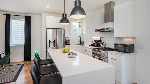 A modern kitchen with white cabinets, a central island, black pendant lights, stainless steel appliances, and a black microwave.