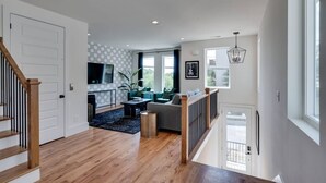 A spacious living area with a wooden staircase, a seating area with a sofa and coffee table, and a large window providing natural light.