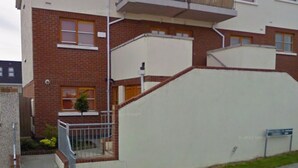 Ein zweistöckiges Wohngebäude mit Ziegelaußenwand, einem Balkon im oberen Stockwerk und einem kleinen Vorgarten.
