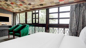 Ein Hotelzimmer mit einem großen Bett, einem grünen Sessel, einem Flachbildfernseher und einem Fenster mit Blick auf Bäume.
