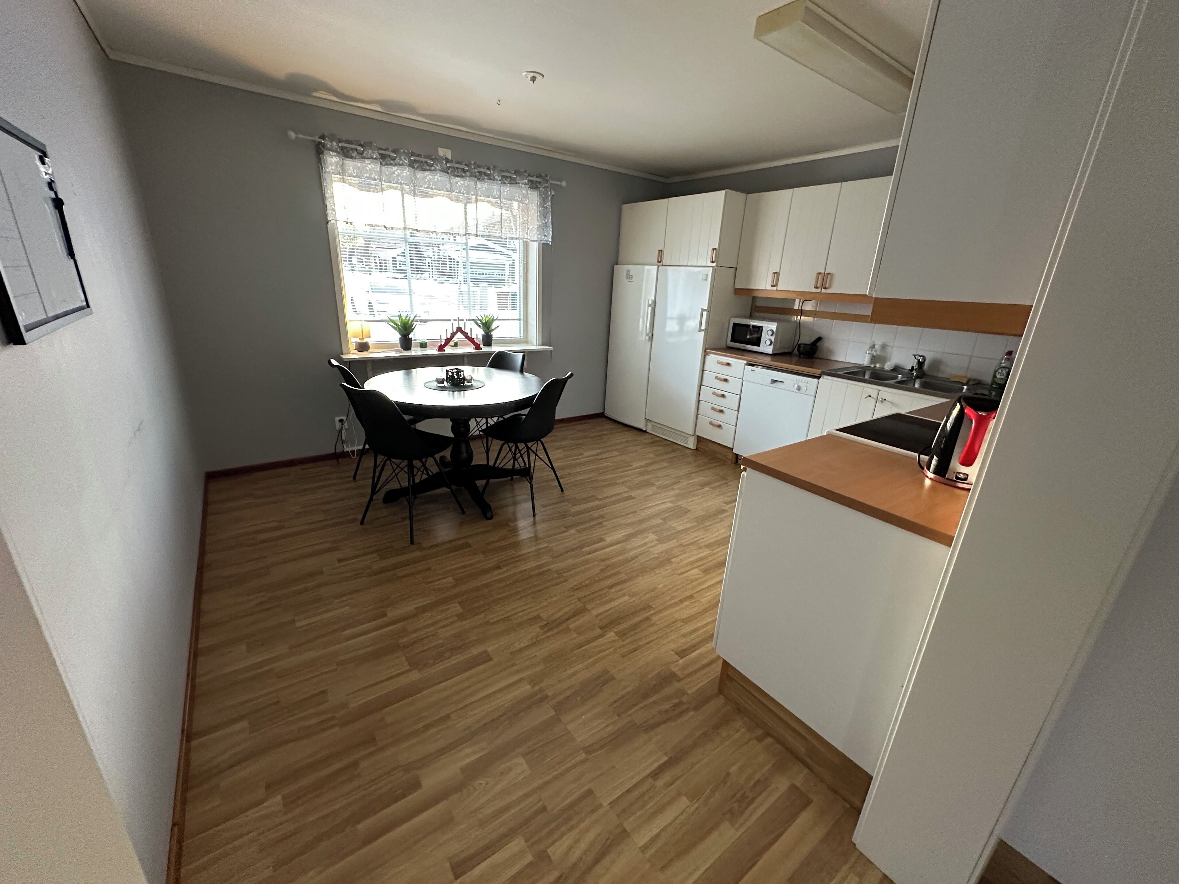 A compact kitchen with white cabinets, a microwave, and a red kettle.