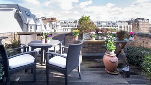 Eine Dachterrasse mit Korbmöbeln, Topfpflanzen und Blick auf die Stadtlandschaft.
