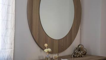 A round mirror with a wooden frame on a wall, a vase with flowers, and a small decorative item with the word "love" on a wooden surface below.