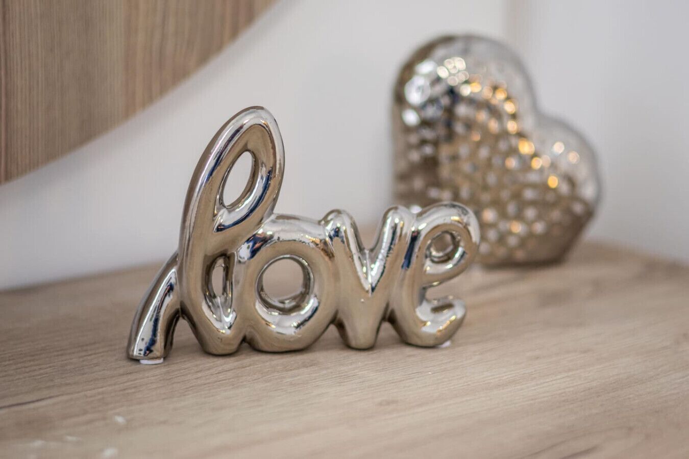 A metallic 'love' sign on a wooden surface with a blurred heart-shaped object in the background.