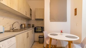 Cocina compacta con lavabo, microondas y un pequeño comedor con dos sillas y una mesa.