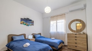 Un dormitorio con dos camas, un tocador, un espejo, una ventana con cortinas y una obra de arte en la pared.
