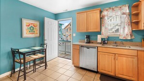 Une cuisine aux murs de couleur turquoise, avec des meubles en bois, un lave-vaisselle et un coin repas comprenant une table et des chaises.