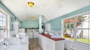 Une cuisine avec des appareils électroménagers blancs, un plancher en bois et une vue sur une maison par la fenêtre.