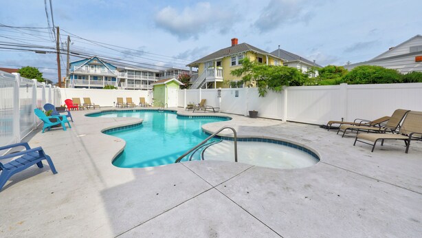 Une piscine avec un petit jacuzzi, entourée de chaises longues et d’une clôture blanche.