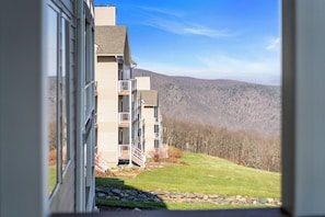 Un immeuble à plusieurs étages doté de balcons, d’un chemin pavé de pierres et offrant une vue sur un paysage vallonné.