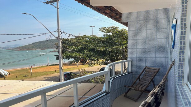 Un balcón con vista a la playa, una pared de azulejos y una silla de madera.