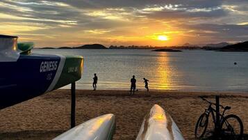 Ein Strand mit Kanus, einem Fahrrad und Menschen, die sich im Abendrot am Wasser vergnügen.