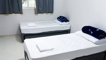 Et hotelværelse med to enkeltsenge, et vindue med gardiner og et flisegulv.