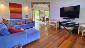 A living room with a blue sofa, a television, a piano, and a dining area with a table and chairs.