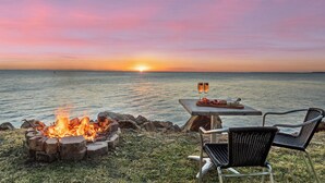 A sunset view over water with a fire pit and outdoor seating. - Absolute waterfront property on rock wall (Amity Point)