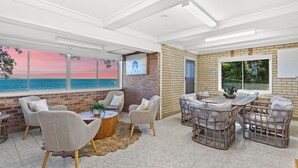 A spacious room with a large window overlooking the sea, a brick wall, and a cozy seating area with wicker furniture. - Absolute waterfront property on rock wall (Amity Point)
