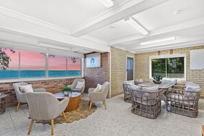 A spacious room with a large window overlooking the sea, a brick wall, and a cozy seating area with wicker furniture.