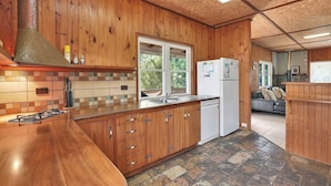 Una cocina de madera con estufa a gas, refrigerador blanco y ventana con vista a la vegetación.