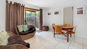 A modern living room with a sofa, dining table, chairs, and a staircase leading to a balcony.