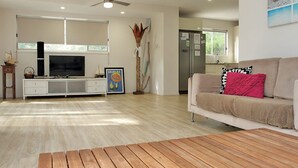 Una sala de estar moderna con un televisor de pantalla plana, un sofá blanco con cojines rojos y negros, una mesa de centro de madera y un ventilador de techo.