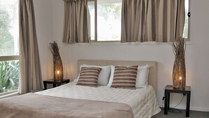 Un dormitorio con una cama grande, dos mesitas de noche con lámparas y una ventana con cortinas.