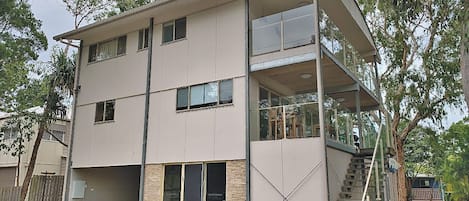 A modern multi-story building with a flat roof, large windows, and a balcony on the upper floor.