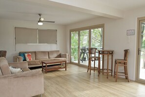 A spacious living room with a large window, a ceiling fan, and a dining area with wooden chairs and a table.