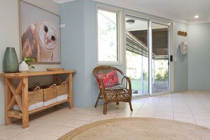 A room with a wooden console table, wicker baskets, a wicker chair with a floral cushion, a large framed owl painting, and a sliding glass door leading to an outdoor area.
