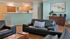 A modern living room with a black leather sofa, wooden coffee table, and a dining area with wooden cabinets and a refrigerator.