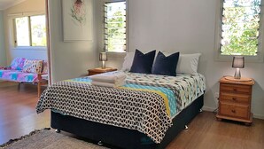 A bedroom with a bed, two bedside tables, a nightstand, a window, and a door leading to another room.