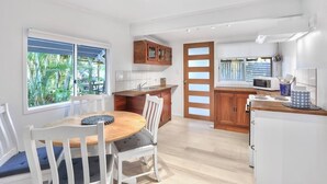 A modern kitchen with white cabinetry, a wooden dining table, and a view of greenery outside.