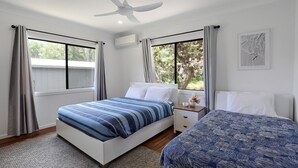 Ein Schlafzimmer mit zwei Betten, einem Deckenventilator und großen Fenstern mit Vorhängen.