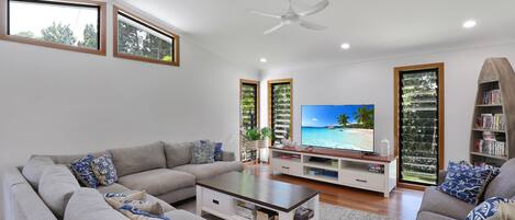 A modern living room with a grey sofa set, a coffee table, a flat-screen TV, and a bookshelf.