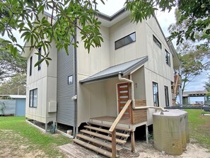 A modern two-story house with a flat roof, a covered porch, and a wooden staircase leading to the entrance.