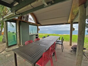 Een terras buiten met een tafel, stoelen, een barbecue en uitzicht op de oceaan.