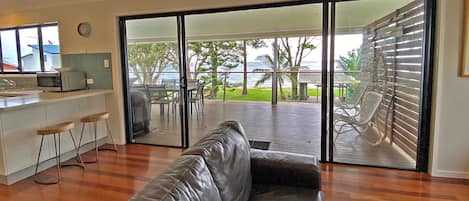 Una sala de estar con un sofá de cuero, una zona de cocina con microondas y un ventanal corredero que da a una terraza exterior con vista al océano.
