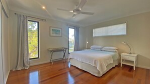 A bedroom with a bed, a desk, a nightstand, a ceiling fan, and large windows.