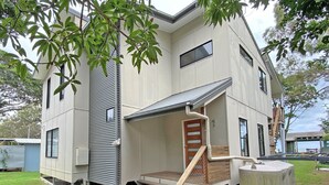A modern two-story house with a flat roof, a covered porch, and a wooden staircase leading to the entrance.